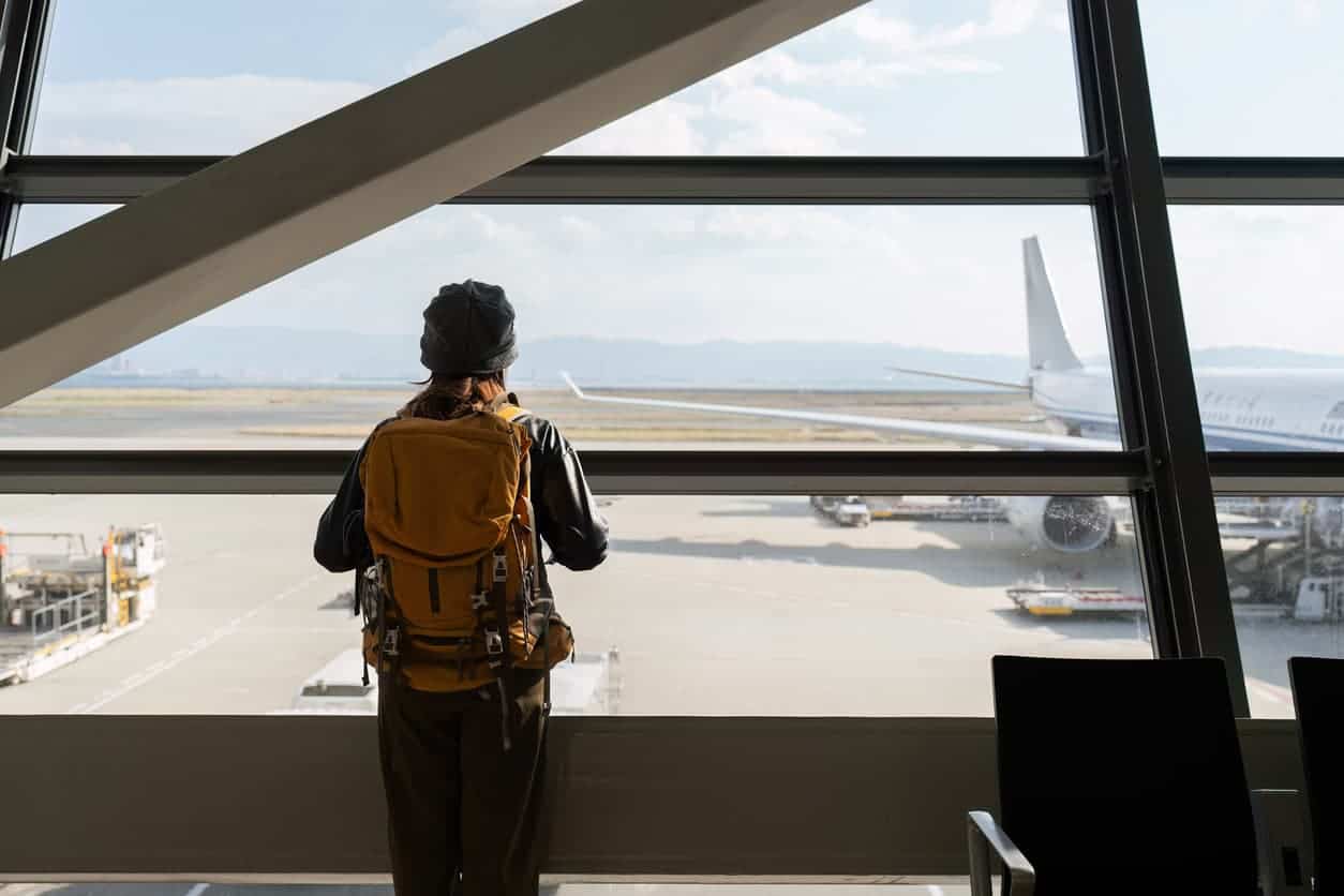 Backpacker traveler looking out airport window at airplane during layover