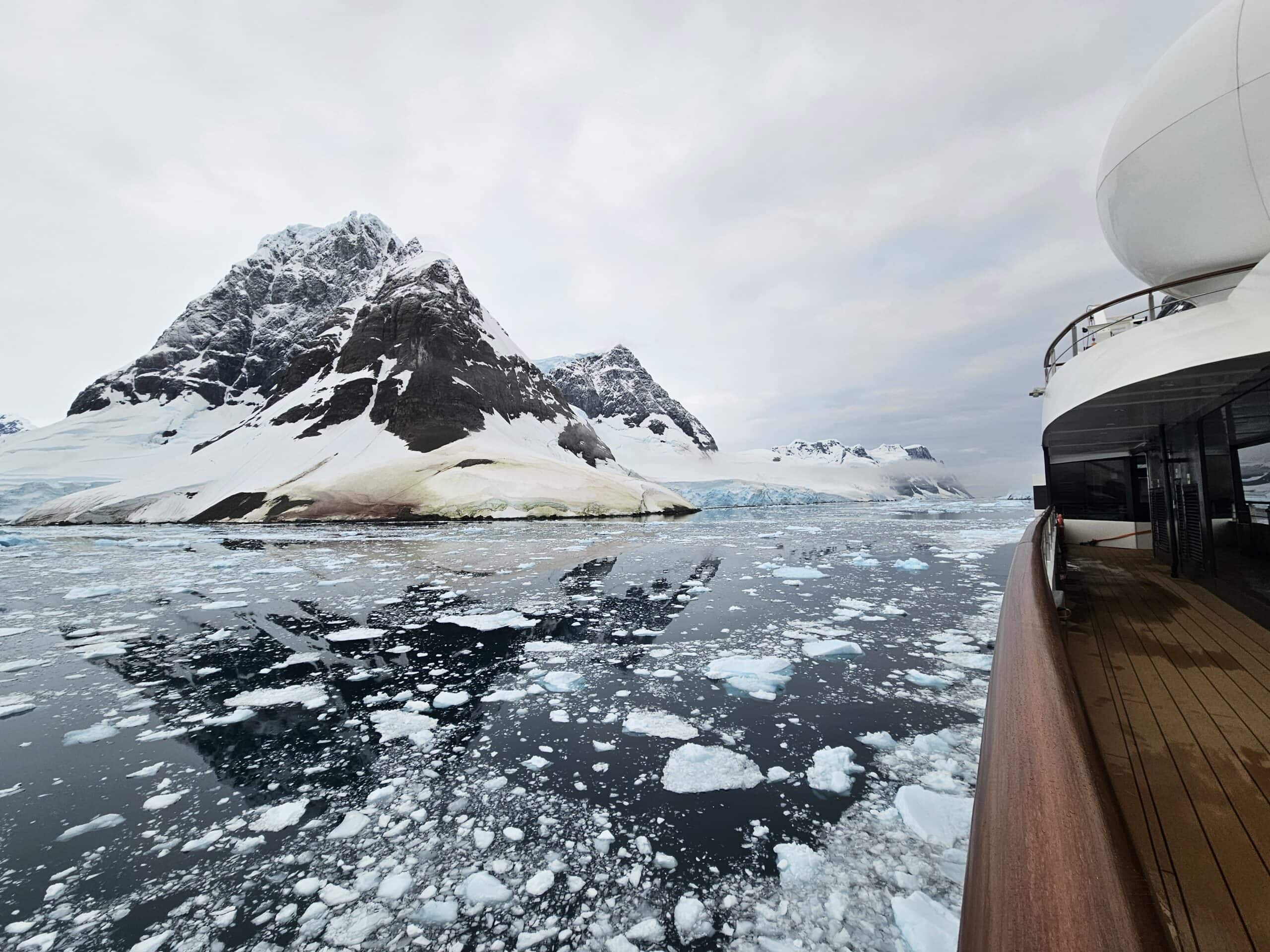 Expedition cruise ship near the Antarctic Peninsula with penguins on ice for the 10xTravel 2027 group trip