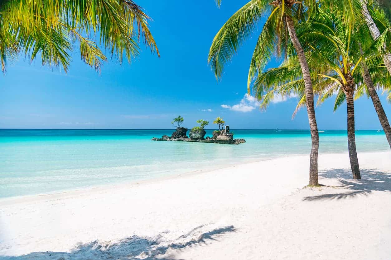 Boracay White Beach with view of Willy’s Rock and palm trees under clear blue sky.