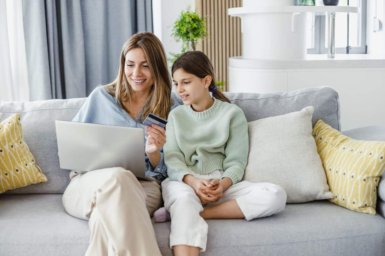 Mother teaching her daughter about online shopping using a laptop and credit card at home
