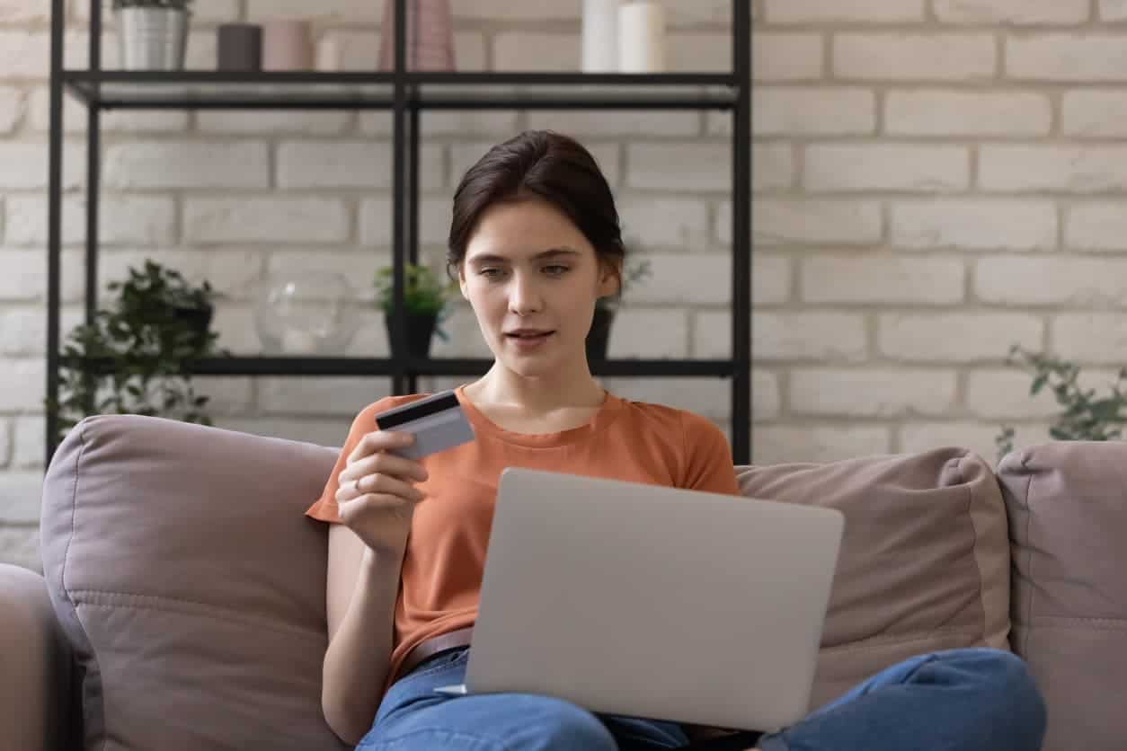 Woman using a laptop while holding a credit card to check account updates online.
