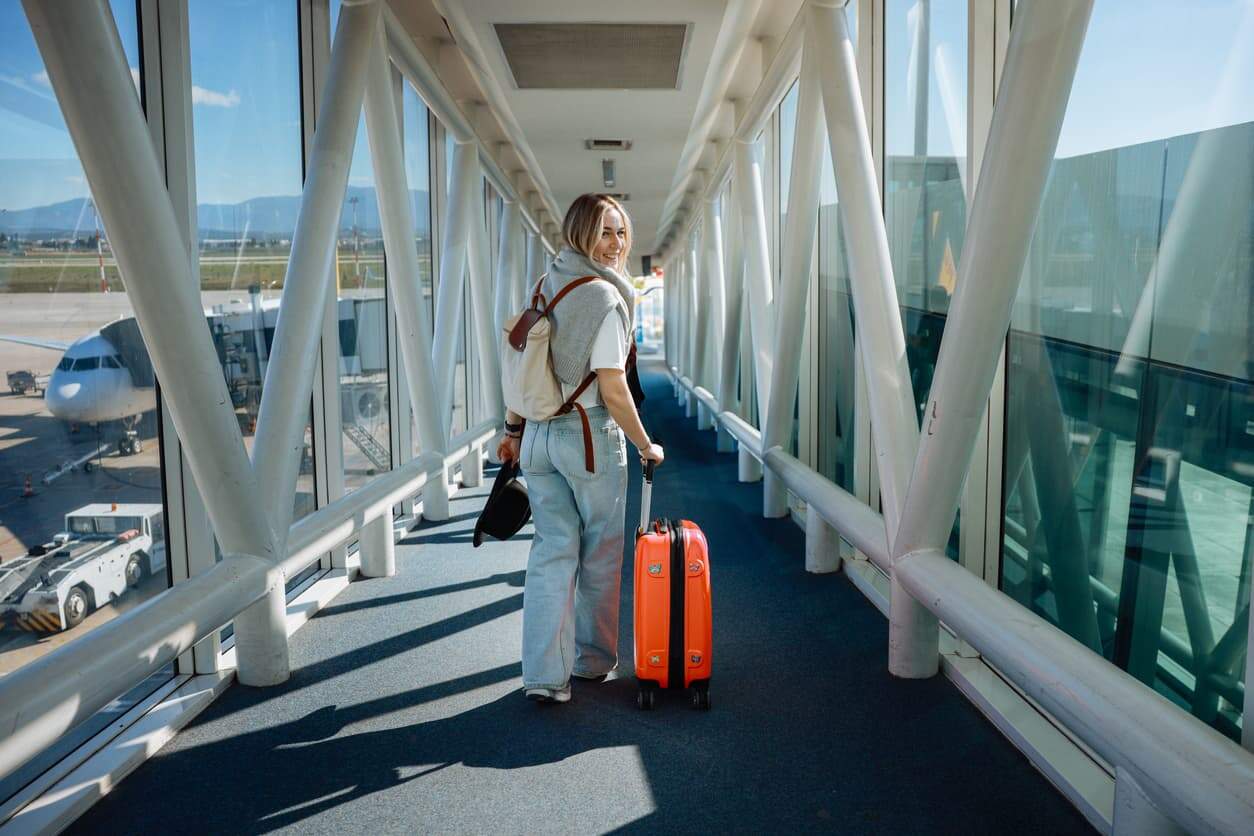 Woman walking through airport boarding gate with suitcase and backpack