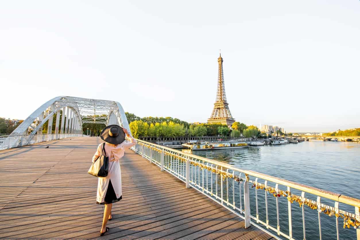 Woman walking across a bridge in Paris with a view of the Eiffel Tower at sunrise