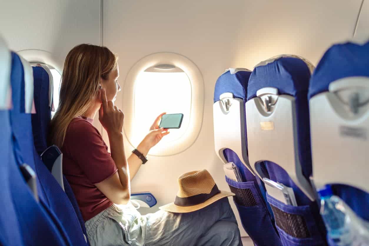 Woman watching her phone by the airplane window during a flight