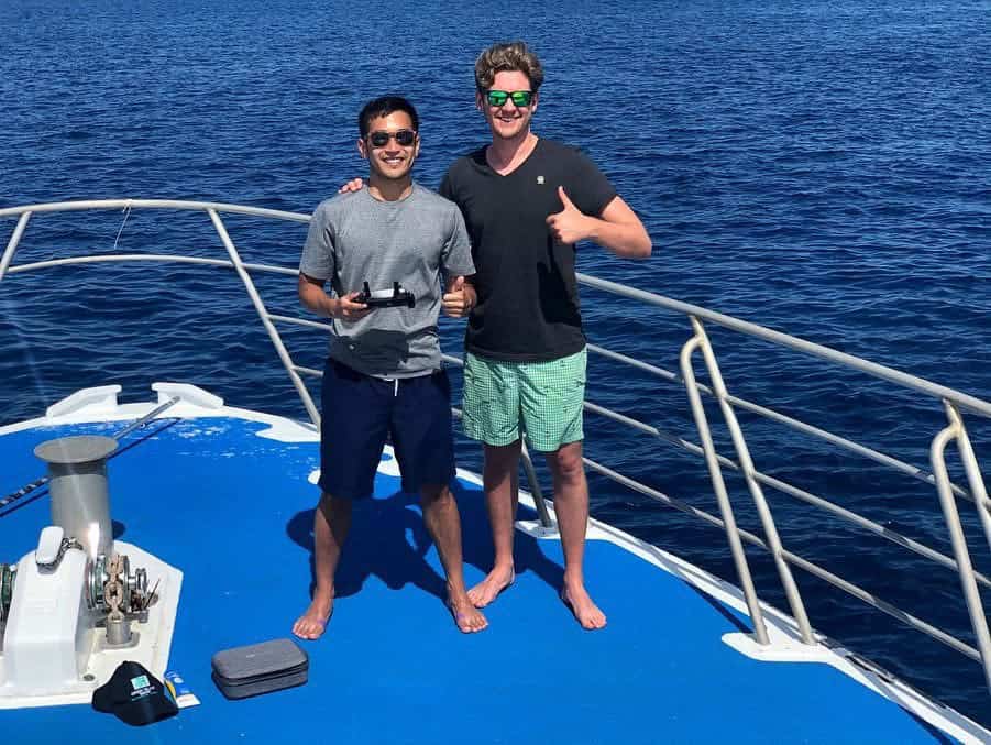Two people smiling on a yacht deck while preparing a drone over the ocean in Bali