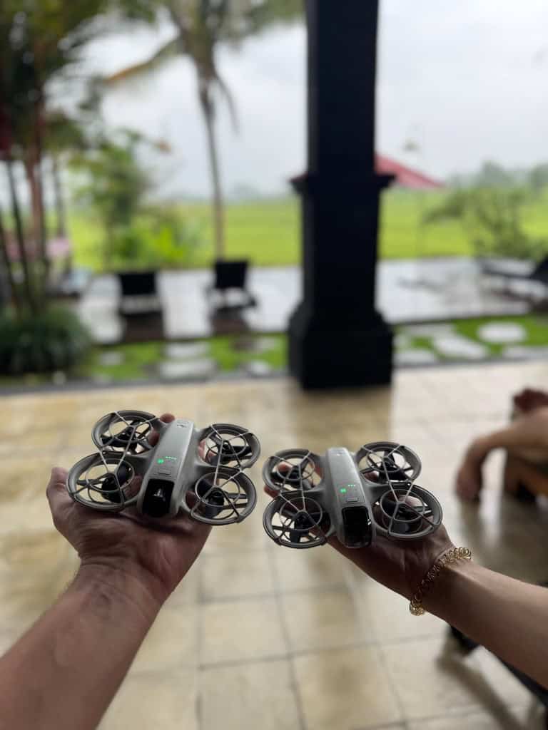 Hands holding two drones ready for flight at a villa overlooking Bali rice fields