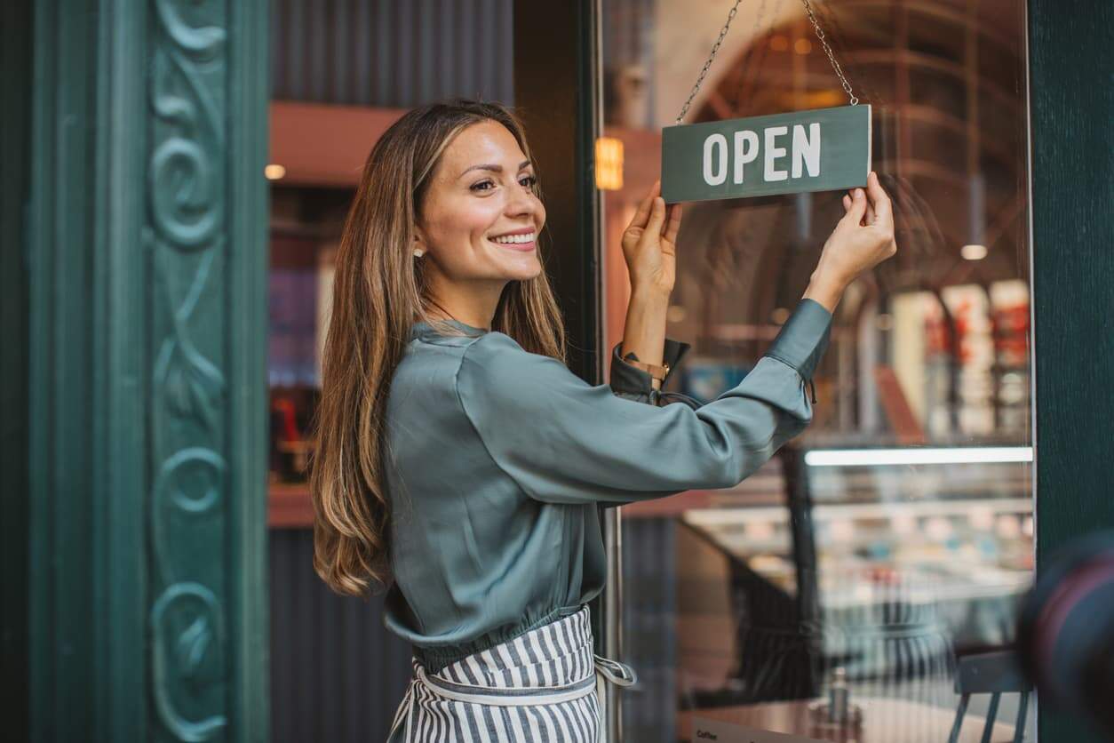 Business owner hanging an open sign on her shop door.
