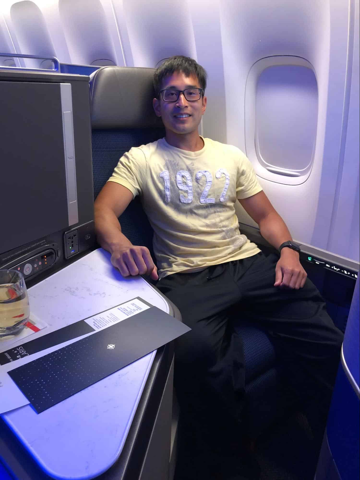 Traveler sitting in a United Polaris business class seat, smiling, with a drink and menu on the tray table during their first points redemption flight.