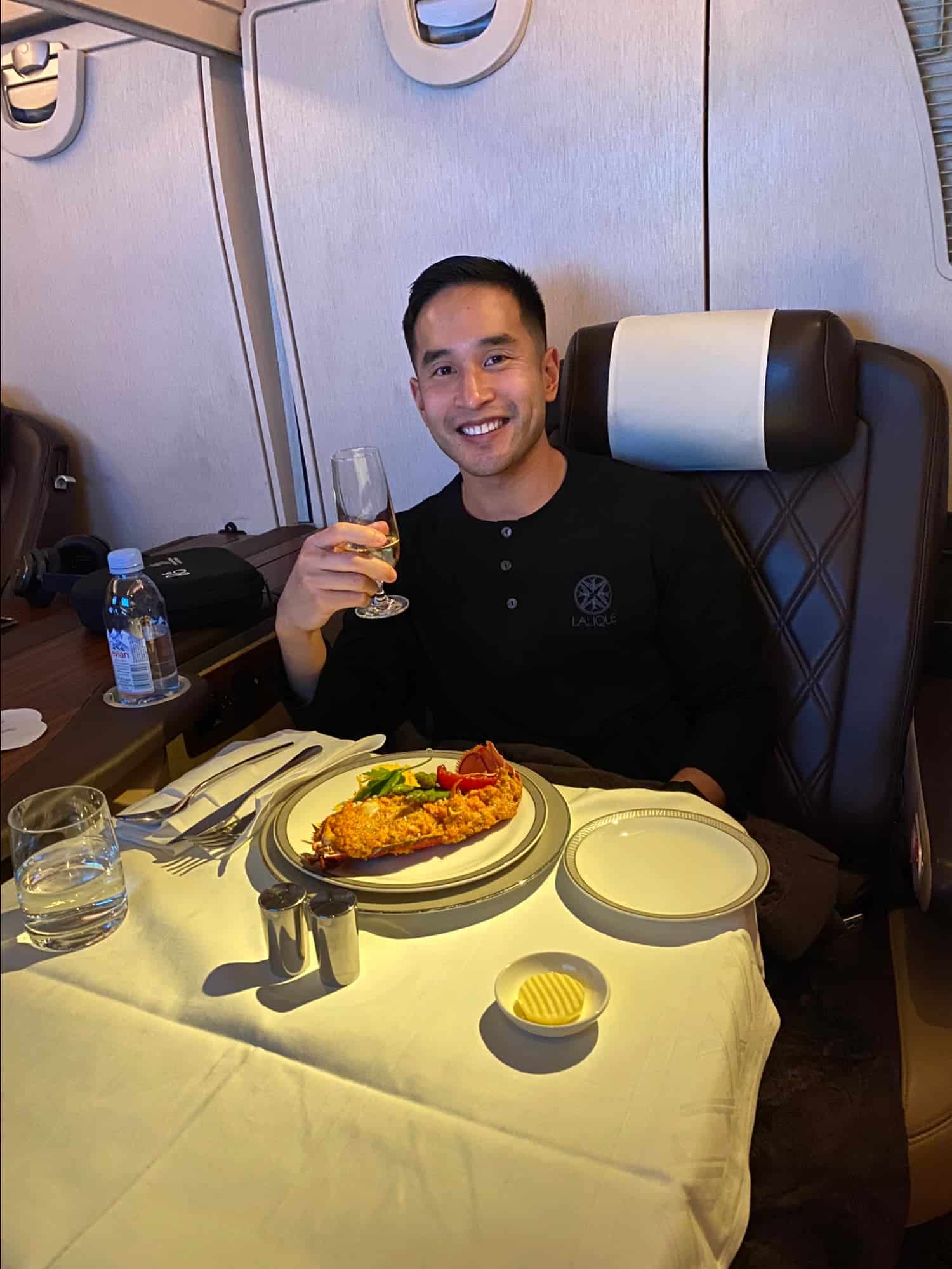 Passenger enjoying lobster thermidor and champagne in a first class airline suite dining setup.