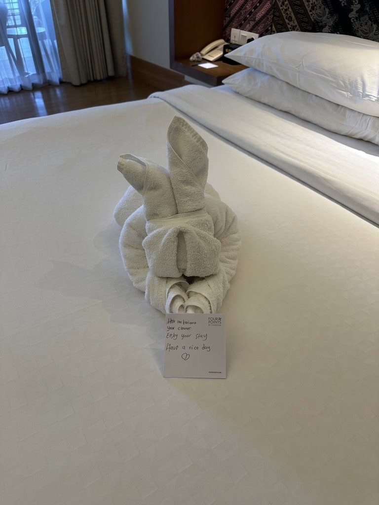 Towel folded into a bunny shape on hotel bed with welcome note at Four Points by Sheraton Bali