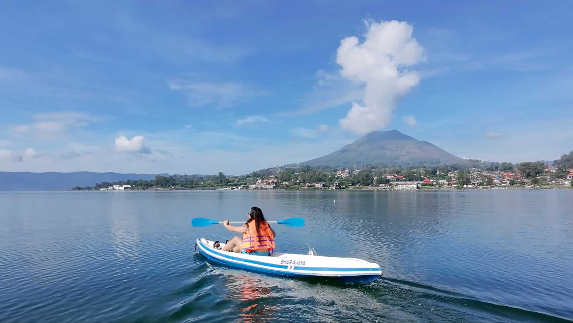 Woman kayaking across Lake Batur with Mount Batur volcano in the distance
