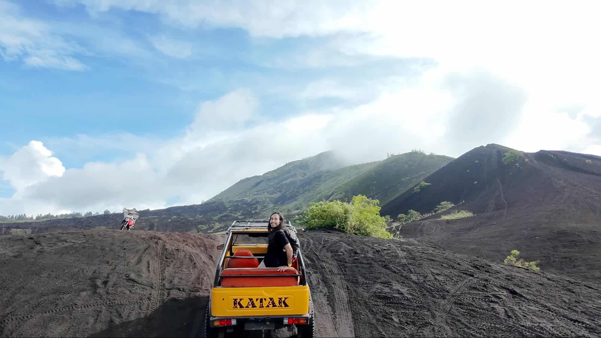 Traveler riding a yellow jeep across black volcanic sand hills at Mount Batur, Bali