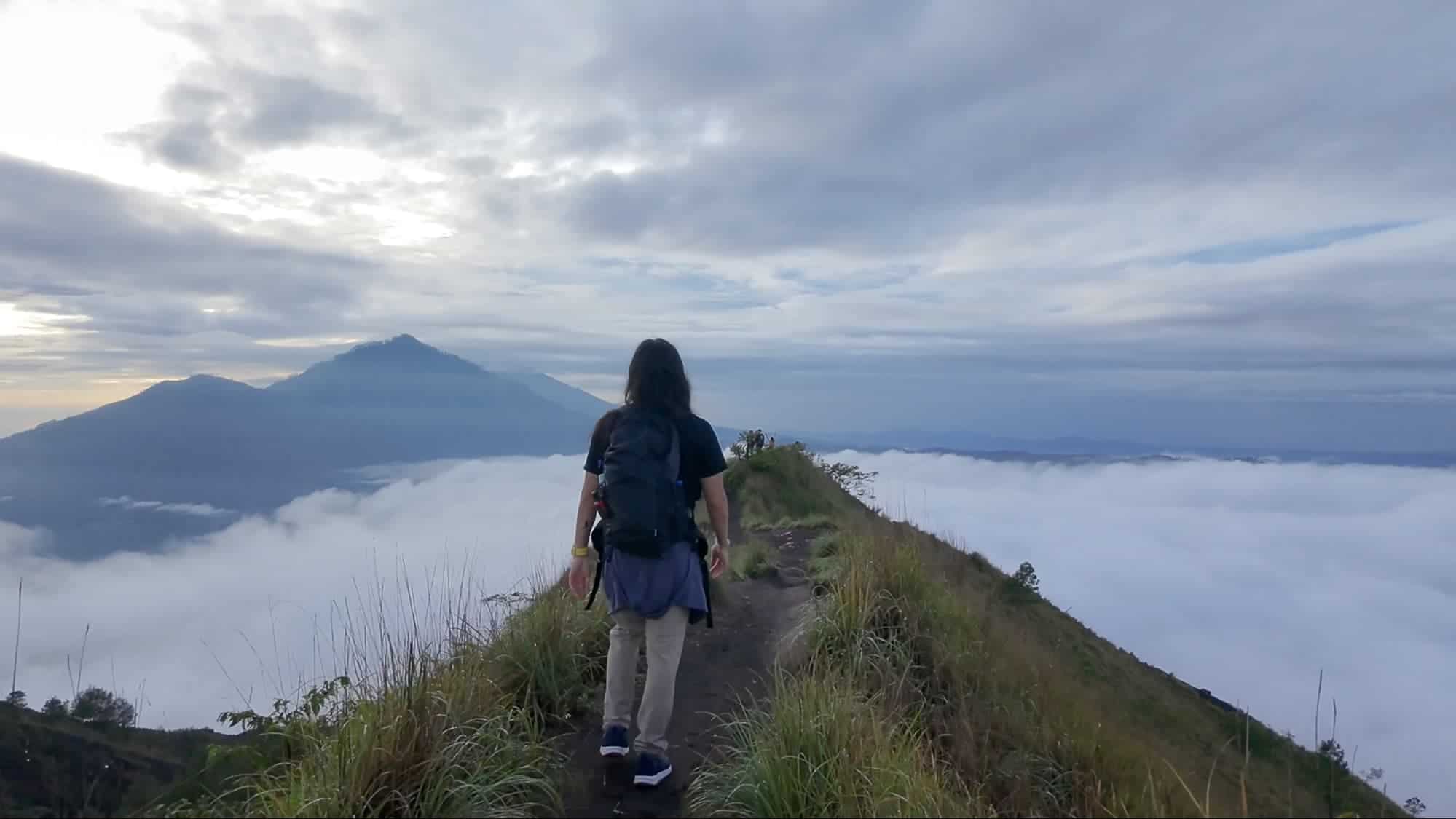 Hiker walking along the ridge above the clouds during sunrise trek at Mount Batur, Bali