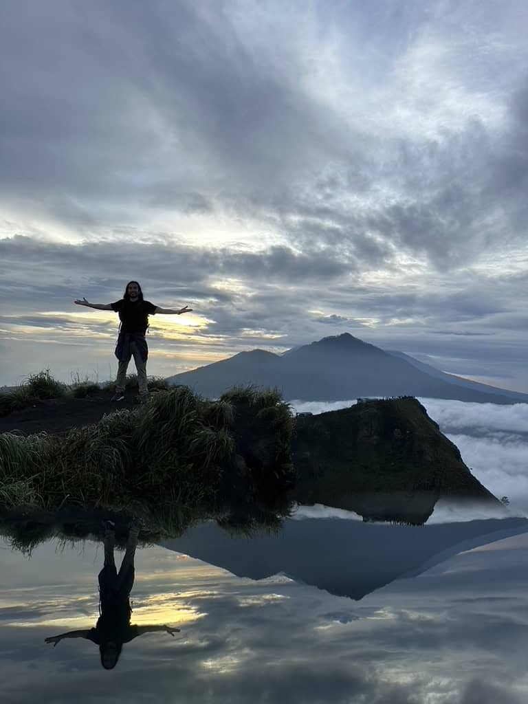 Traveler posing at sunrise with mountain reflection in water at Mount Batur, Bali