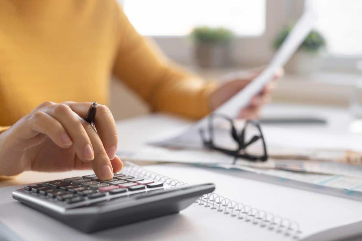 Person using a calculator and reviewing documents while calculating taxes at a desk.