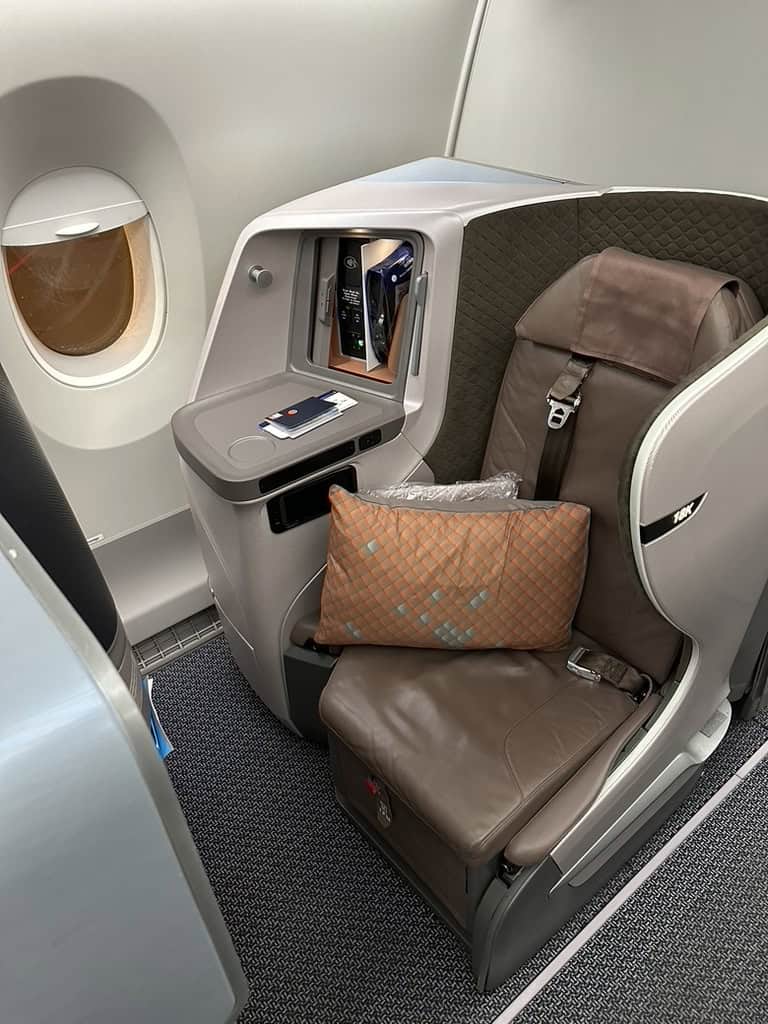 Singapore Airlines business class seat 10K by the window with pillow and passport on side console