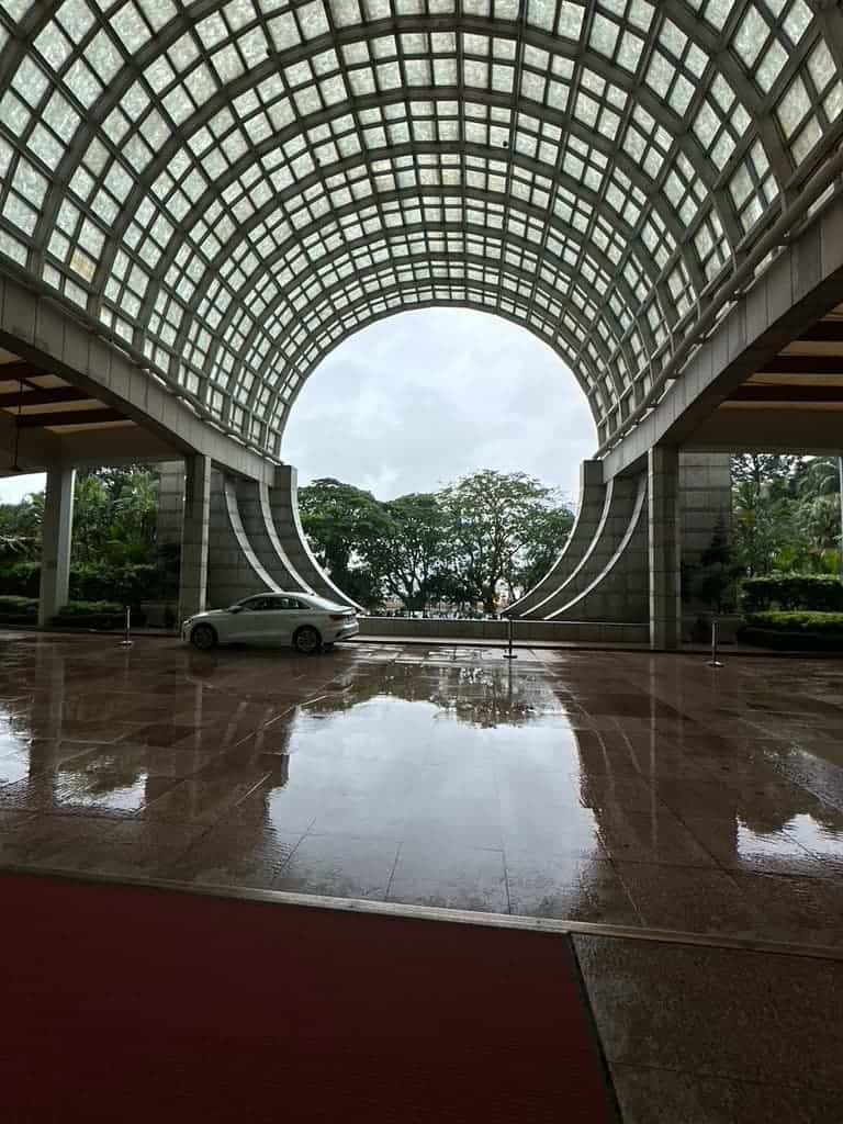 Modern hotel entrance with a curved glass dome and reflective marble floor on a rainy day in Singapore