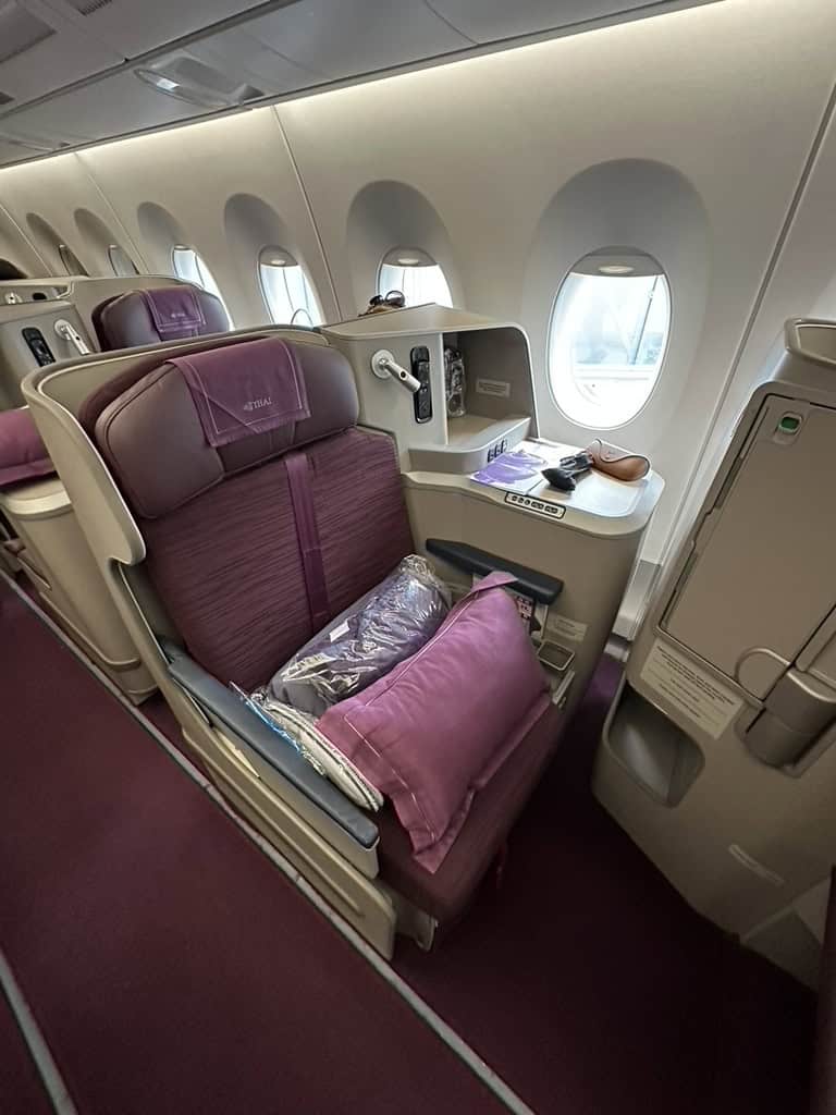 Thai Airways A350 business class window seat with purple upholstery, pillow, and amenities arranged before takeoff.
