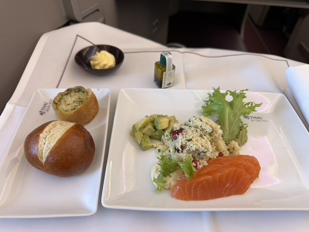 Thai Airways business class appetizer with smoked salmon, couscous salad, avocado, bread roll, and butter served on a white tray.