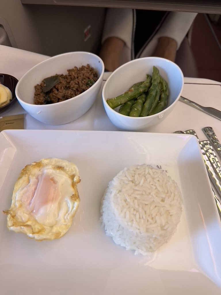 Thai Airways business class meal with rice, fried egg, Thai basil beef, and asparagus served in white dishes.