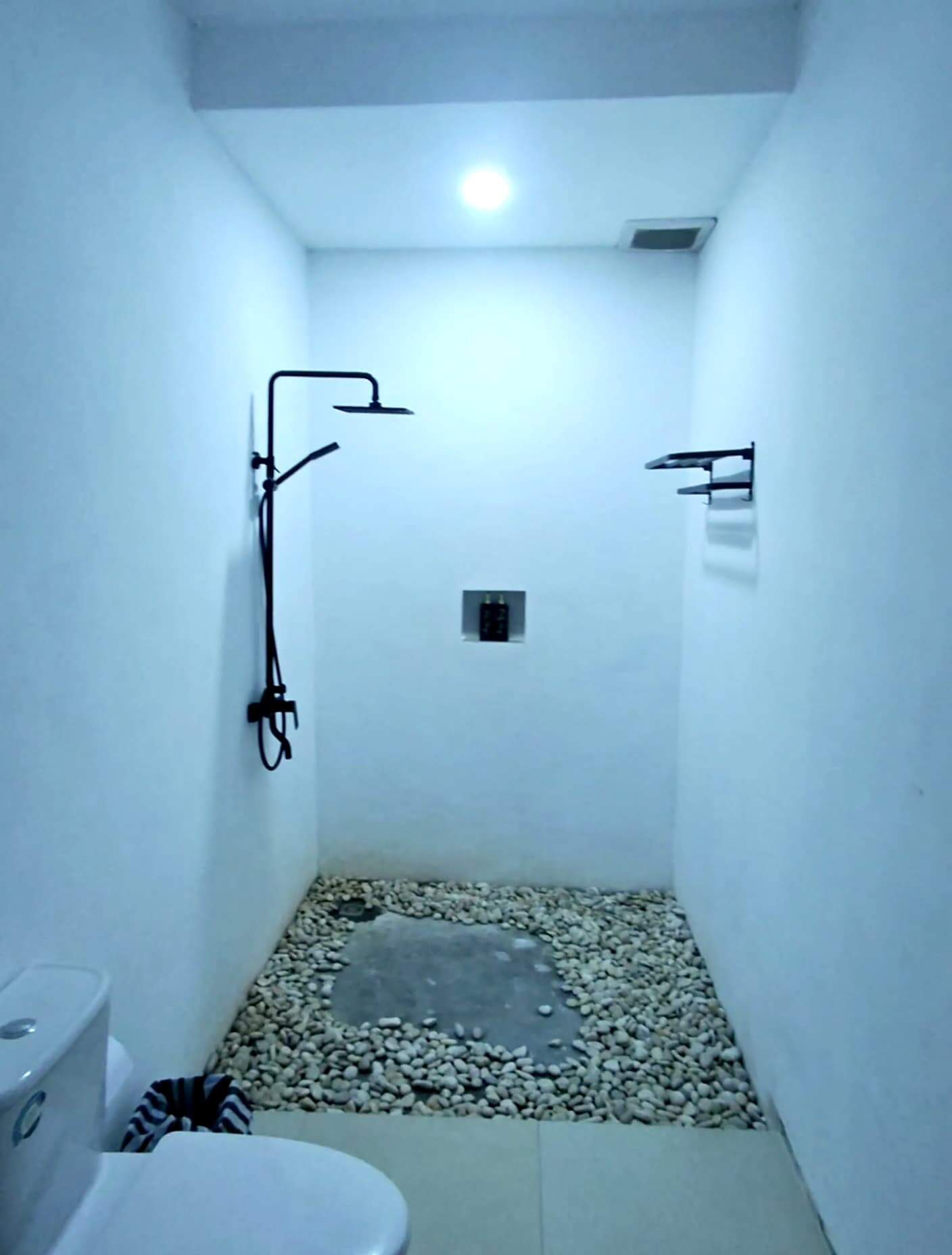 Minimalist bathroom with pebble flooring and modern rain shower at Volcano Garden View Bali