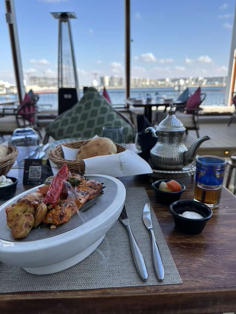 Outdoor seaside dining setup with grilled seafood and Moroccan tea at Yas Bay Waterfront