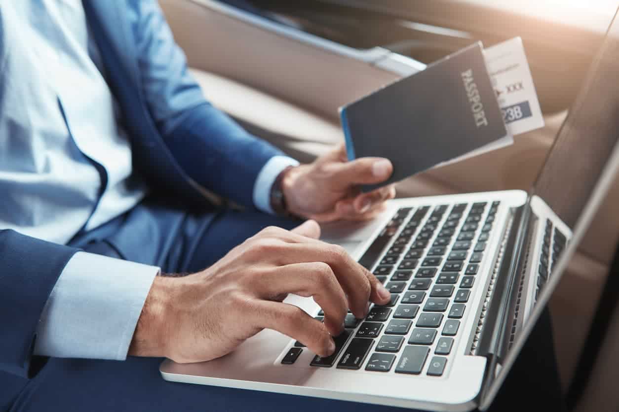 business traveler using a laptop while holding a passport and boarding pass