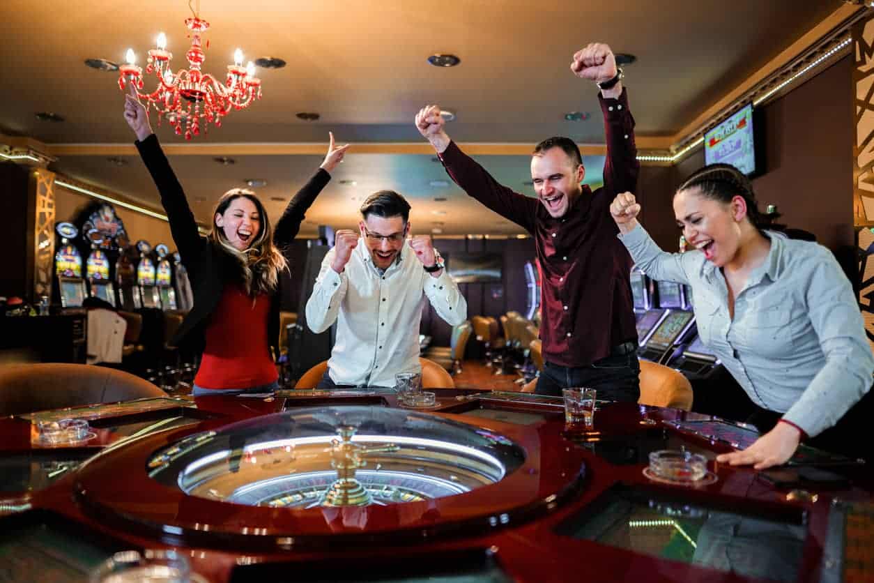 Group of friends cheering around a roulette table after winning in a casino.