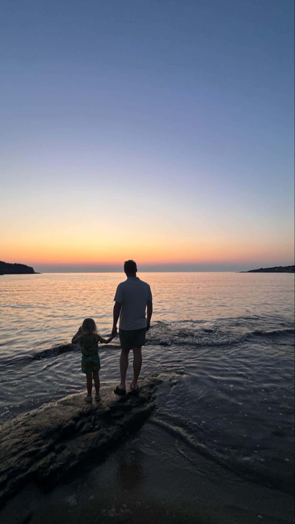 Bryce Conway holding his daughter's hand while watching the sunset by the ocean.