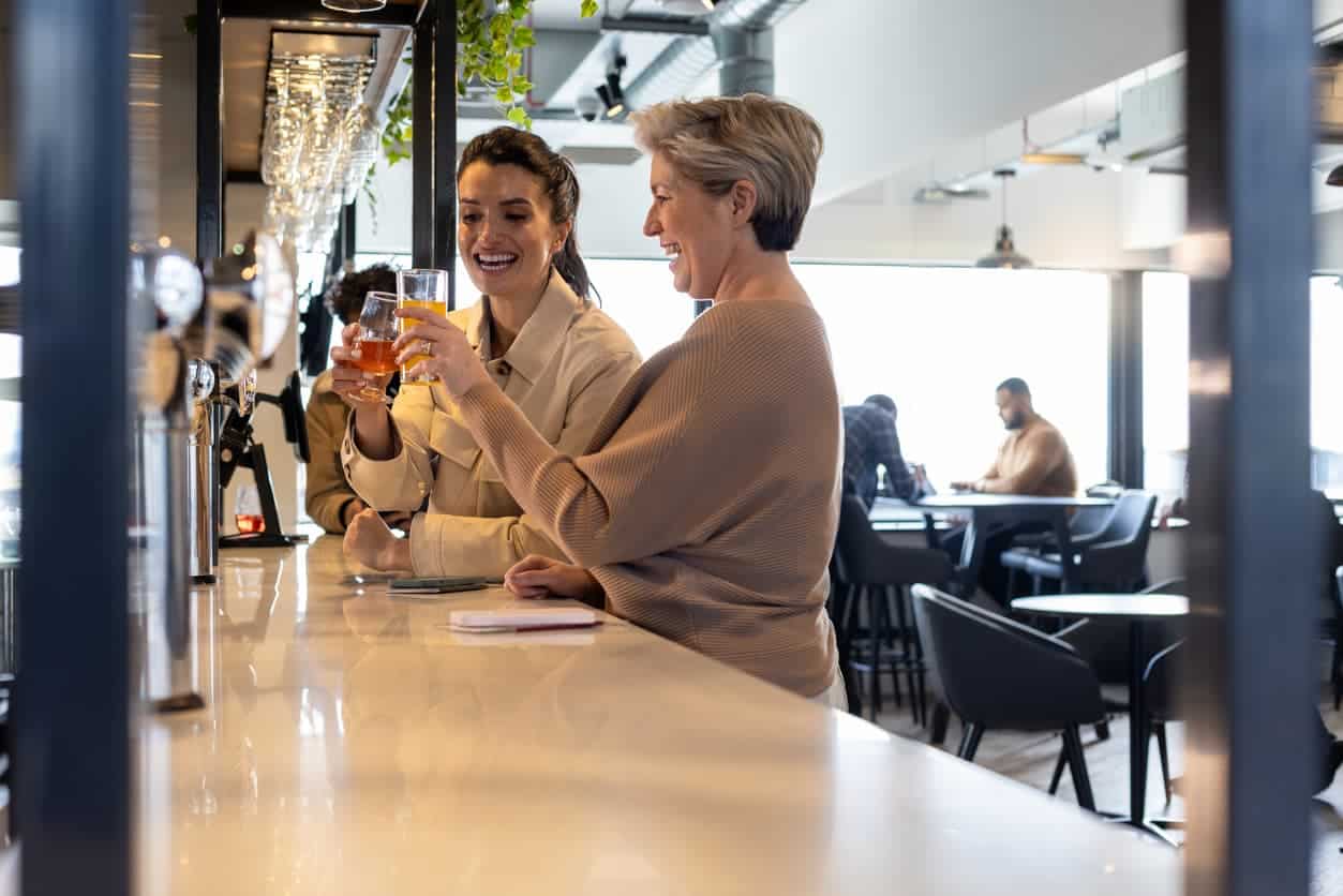 Two women enjoying drinks and toasting together at an airport lounge bar before a flight.