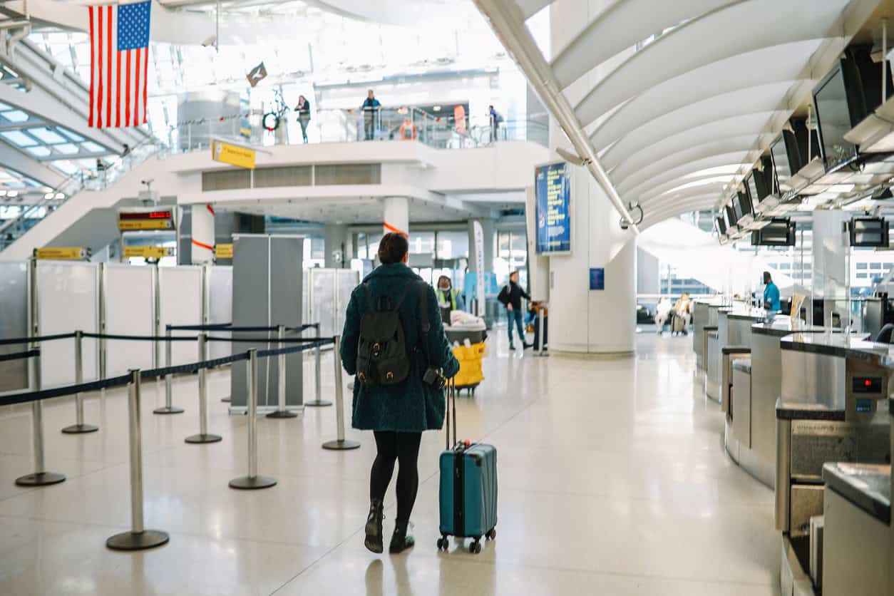 Traveler walking through an airport terminal pulling a suitcase toward security.