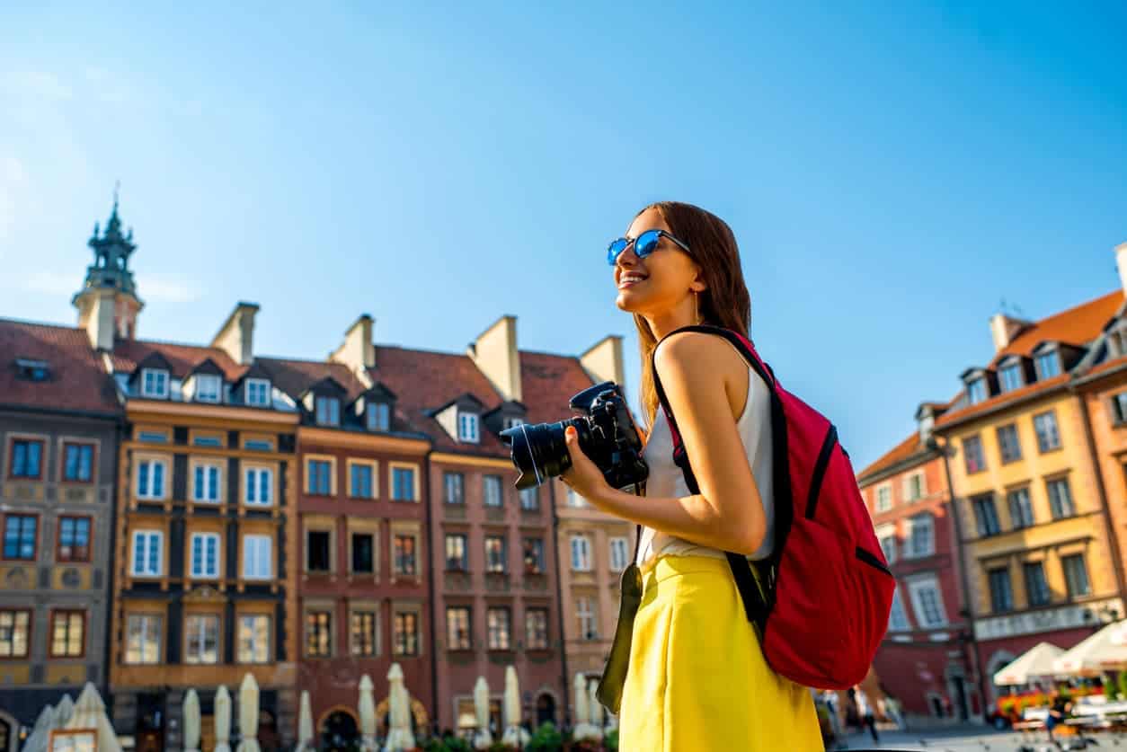 Woman with a camera and backpack sightseeing in Warsaw’s Old Town on a sunny day.