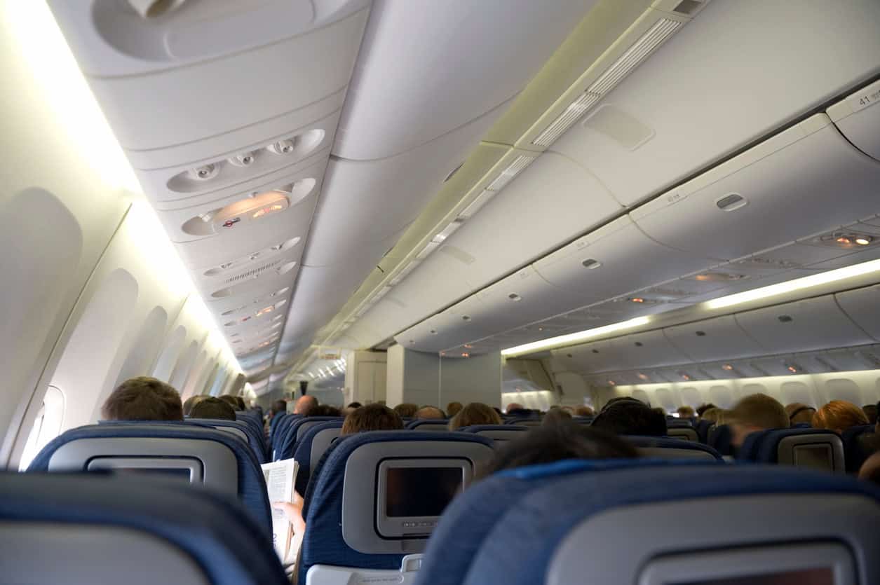 view of an airplane cabin with passengers seated in economy class and overhead bins visible