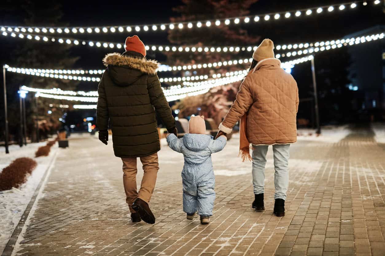 Family walking together on a winter evening under festive string lights.