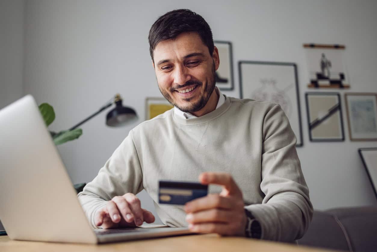 man smiling while using a credit card to book travel online on his laptop