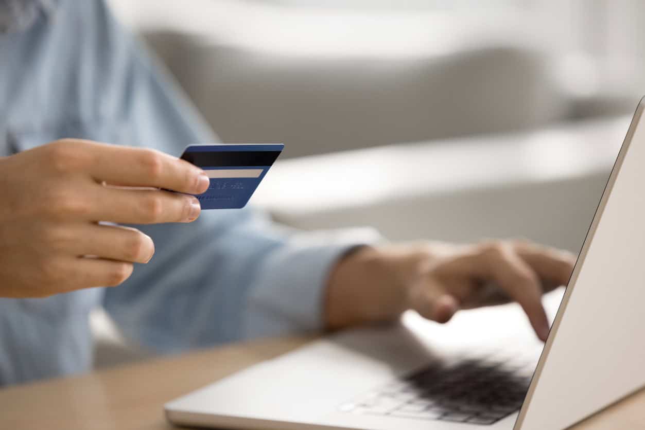 Holding a credit card while typing on a laptop during an online purchase.