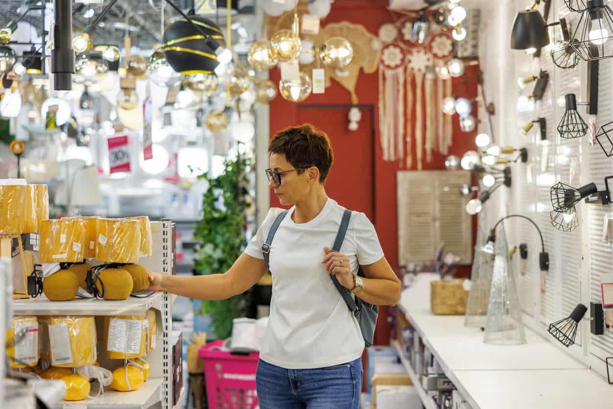 Woman browsing and comparing lighting fixtures while shopping in a home goods store.
