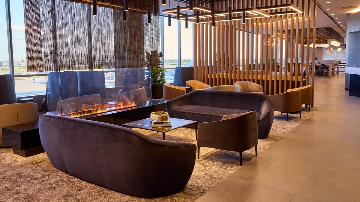 American Airlines Flagship Lounge fireplace seating area at Philadelphia International Airport, featuring modern lounge chairs, floor-to-ceiling windows, and a runway view.