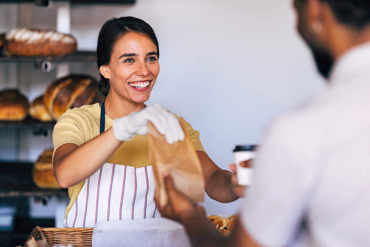 Bakery owner handing a paper bag with baked goods to a customer at the counter