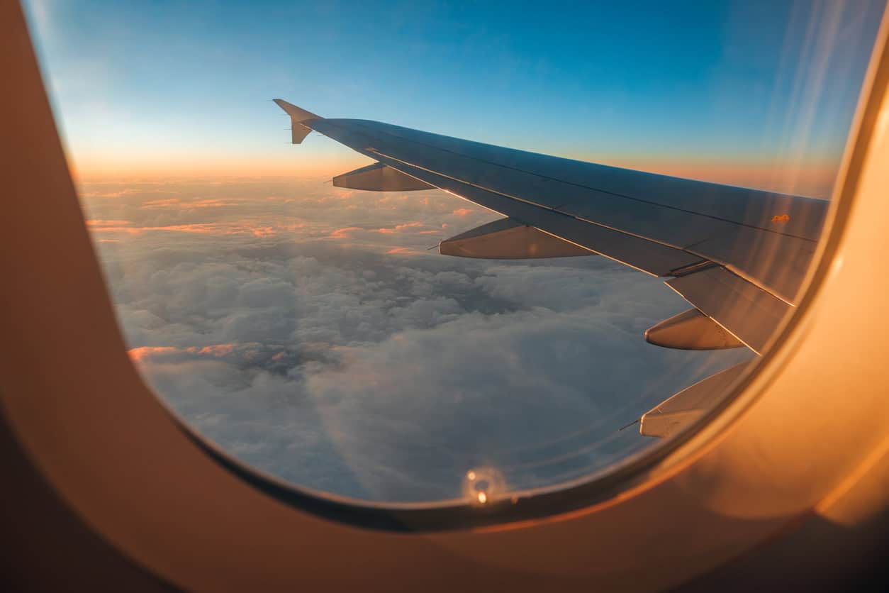 View from an airplane window showing the aircraft wing at sunrise above a blanket of clouds.