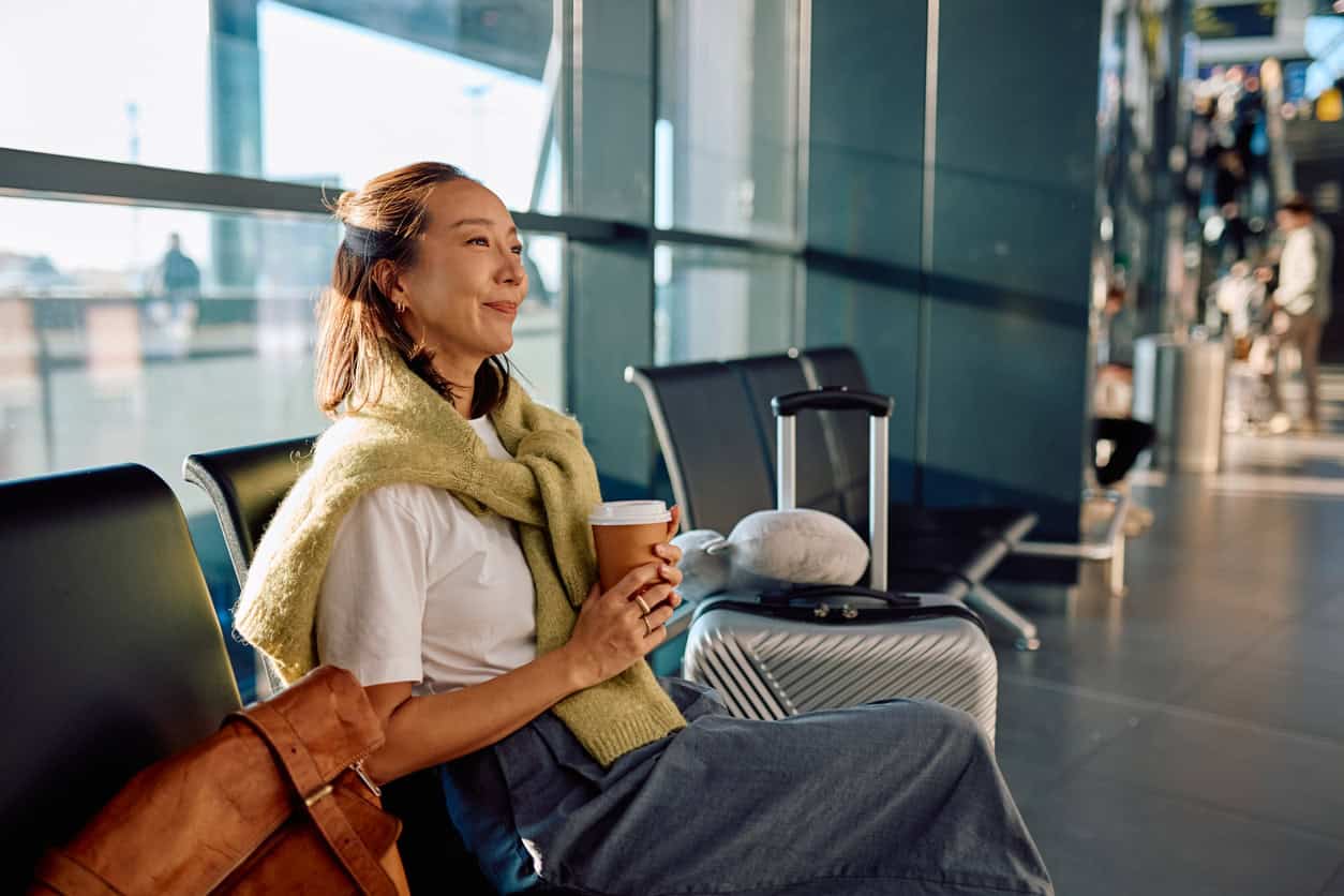 Traveler sitting in an airport terminal with luggage and a coffee, planning a trip and making the most of airline miles and points.
