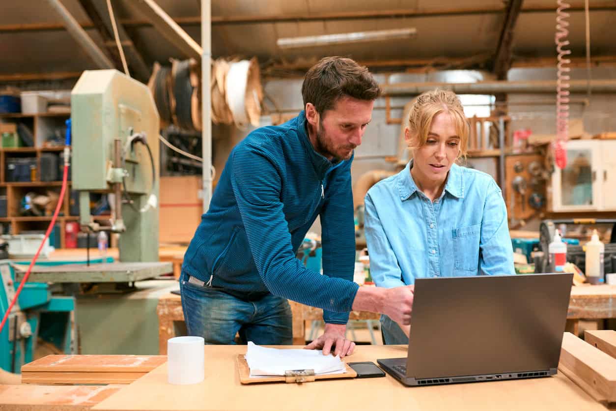 Two small business owners reviewing orders on a laptop in a workshop