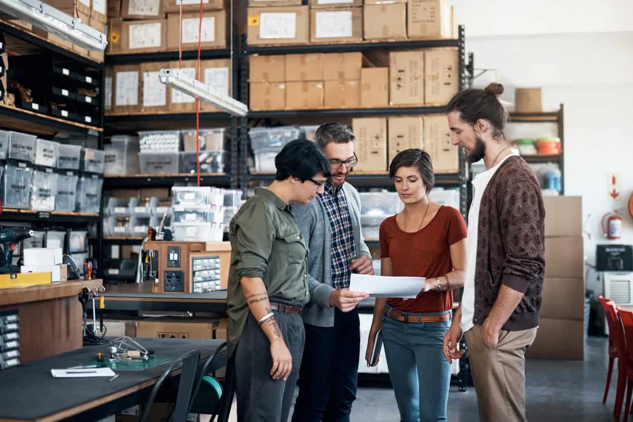 Small business team reviewing paperwork together inside a warehouse with shelves of boxes and inventory