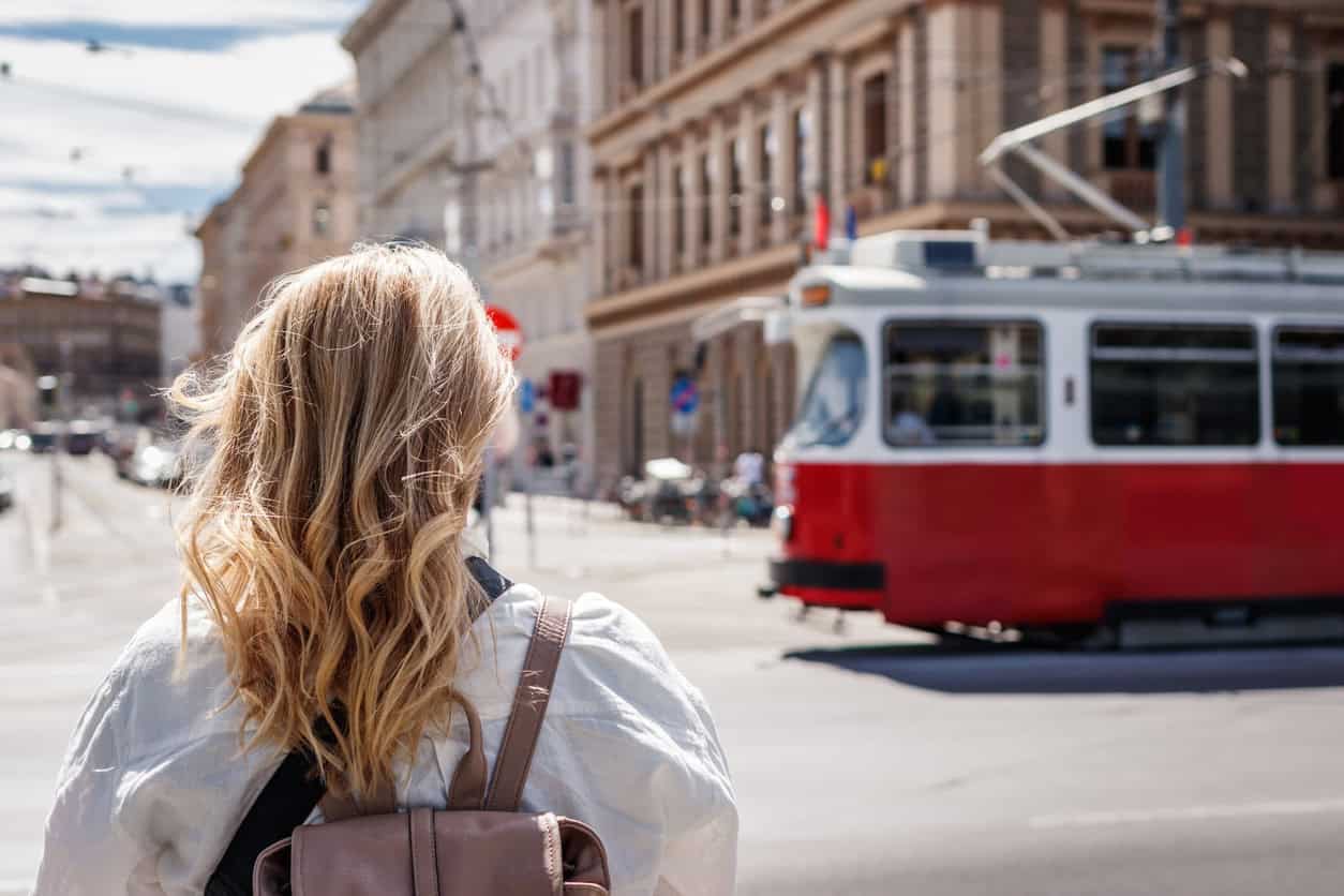traveler standing on a Vienna street watching a red tram pass through the historic city center