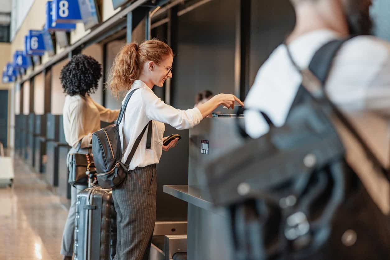Business traveler using a self-service check-in kiosk at an airport counter with carry-on luggage