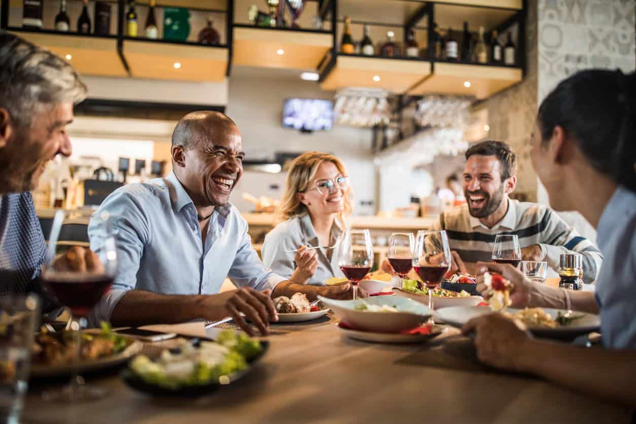 Group of coworkers enjoying dinner together at restaurant table with food and drinks, laughing during team meal