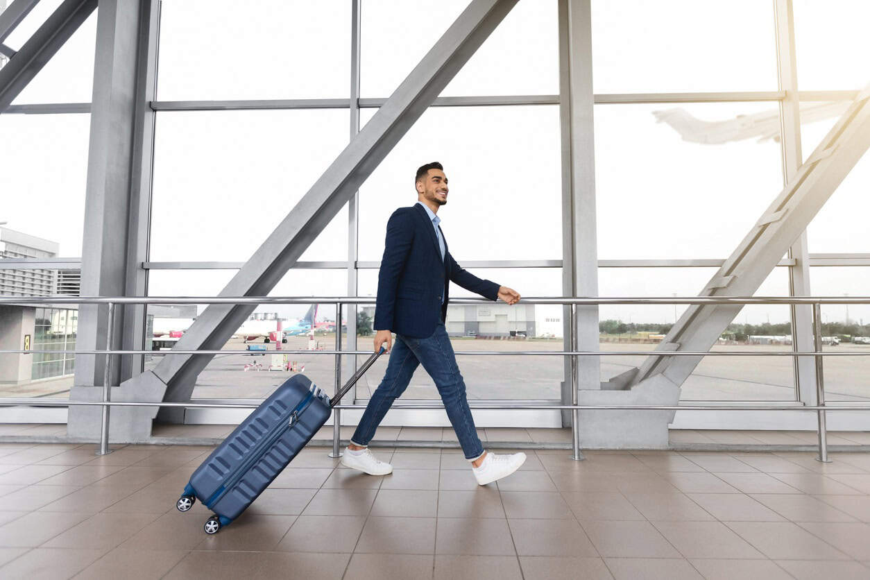 Business traveler walking through airport terminal pulling a rolling suitcase
