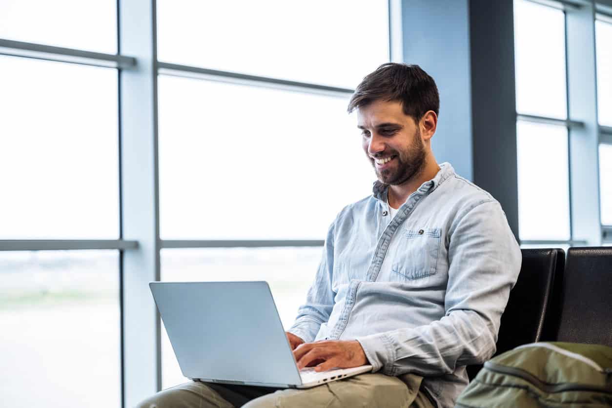 Business traveler sitting at airport gate using laptop while waiting for flight during work trip travel day