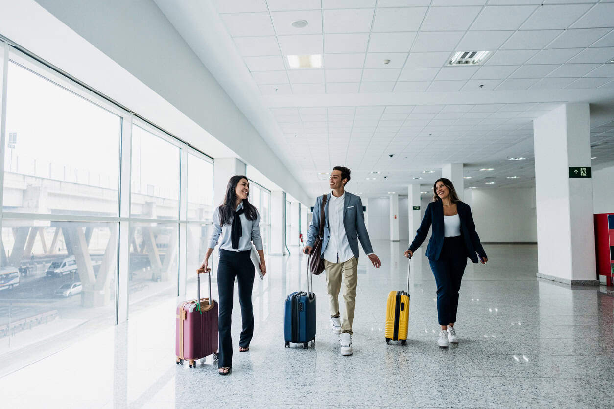 Business travelers walking through airport terminal with rolling suitcases during work trip travel day