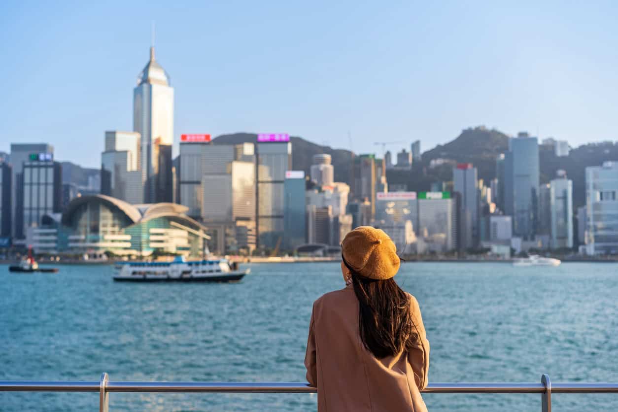 Traveler overlooking Victoria Harbour with the Hong Kong skyline in the background on a clear day, highlighting the city’s waterfront and skyscrapers.
